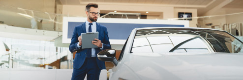 Elegancki mężczyzna w garniturze z notatnikiem ocenia samochód w salonie dealerskim.