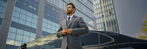 Mężczyzna w garniturze stojący przy nowoczesnym samochodzie na tle biurowców – symbol nowoczesnego biznesu i mobilności