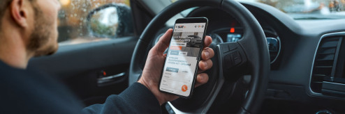 Mężczyzna w samochodzie przeglądający ofertę wynajmu aut na stronie SIXT Drive Smart na ekranie smartfona