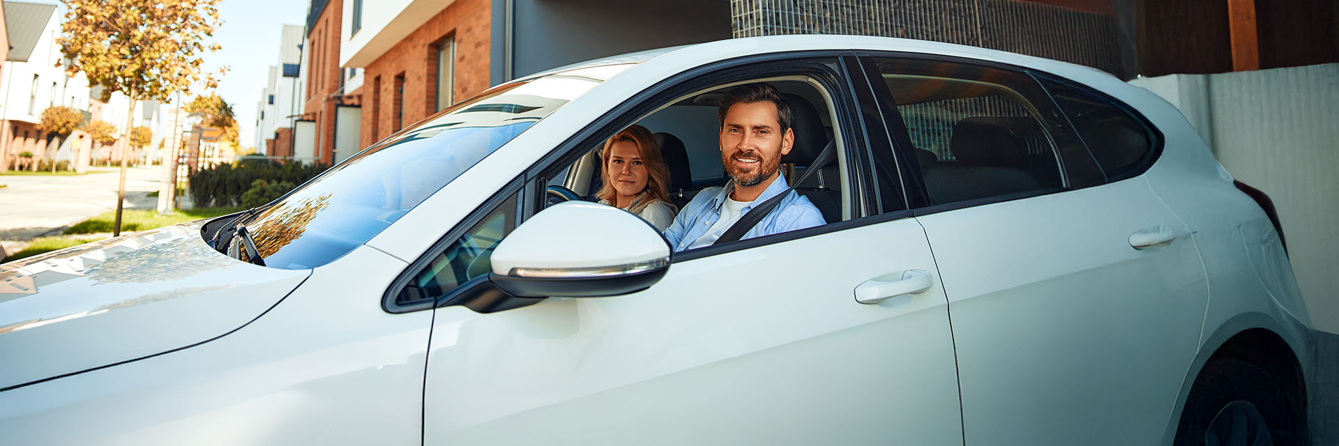 Mężczyzna i kobieta siedzący w białym samochodzie – uśmiechnięci, gotowi do jazdy, przedstawiający koncepcję korzystania z auta na abonament.