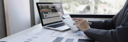 Osoba trzymająca kalkulator i długopis przy laptopie z otwartą stroną SIXT – analiza kosztów zakupu i wynajmu samochodu.