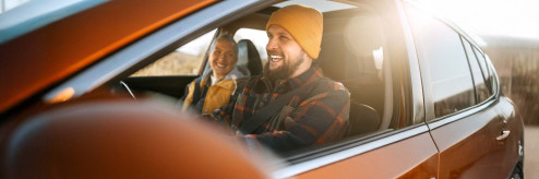 Uśmiechnięty kierowca z pasażerem w samochodzie podczas jesiennej podróży.