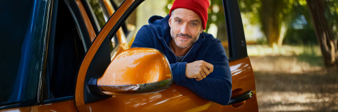 Mężczyzna oparty o otwarte drzwi pomarańczowego samochodu w naturalnym otoczeniu