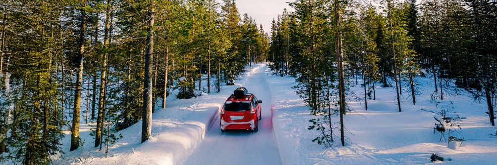 Samochód jadący zimową drogą wśród ośnieżonych drzew – bezpieczna jazda dzięki wynajmowi auta z odpowiednimi oponami.