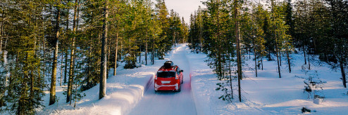 Samochód jadący zimową drogą wśród ośnieżonych drzew – bezpieczna jazda dzięki wynajmowi auta z odpowiednimi oponami.