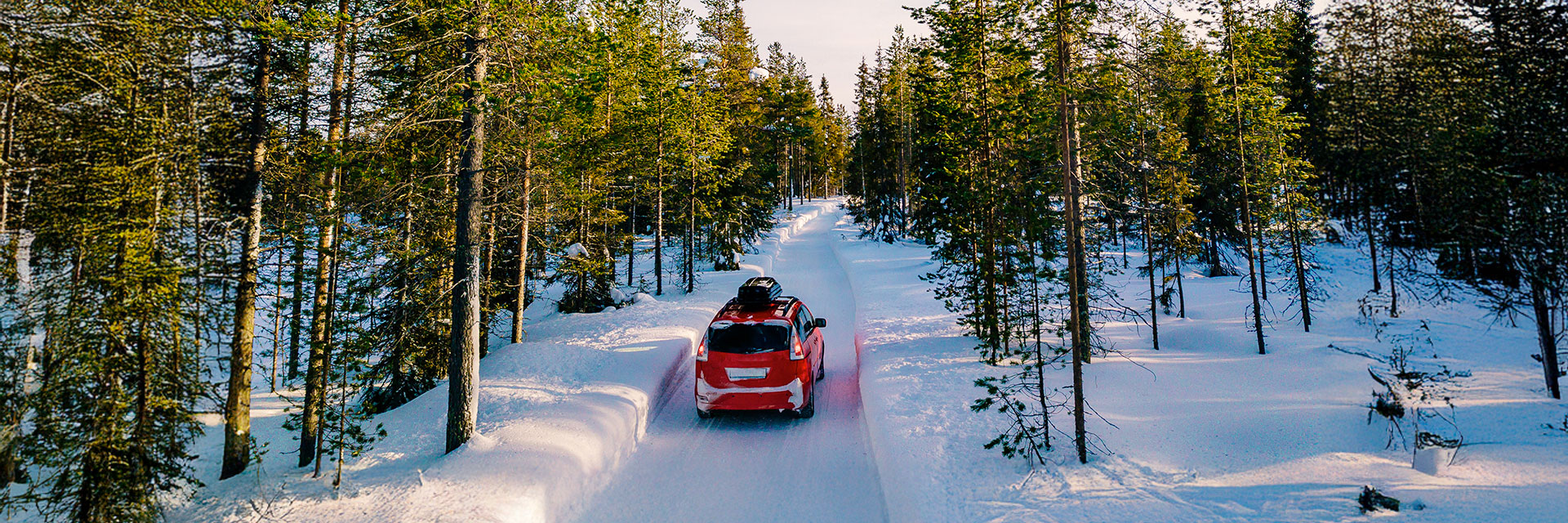 Samochód jadący zimową drogą wśród ośnieżonych drzew – bezpieczna jazda dzięki wynajmowi auta z odpowiednimi oponami.