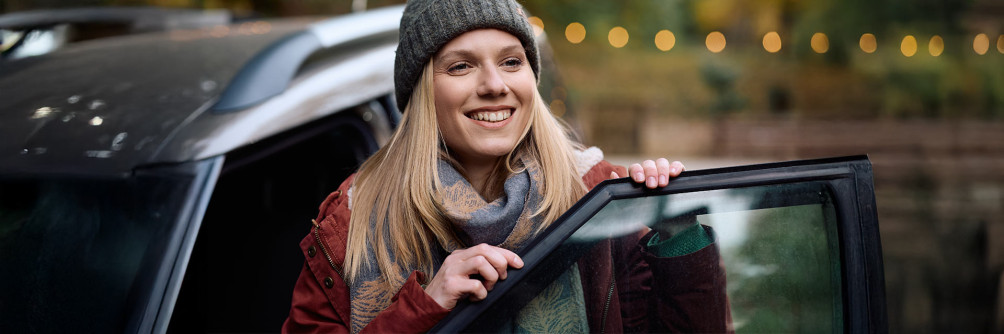 Uśmiechnięta kobieta wysiadająca z samochodu – noworoczne postanowienia motoryzacyjne i wynajem długoterminowy SIXT DriveSmart.