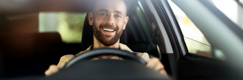 Uśmiechnięty kierowca prowadzi samochód w słoneczny dzień – wynajem auta SIXT DriveSmart